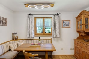 A dining area with a wooden table, bench seating, a window with curtains, a cabinet, and a ceiling light fixture.
