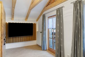 A room with a large flat-screen TV mounted on a wooden panel, a window with curtains, and a radiator.