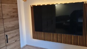 A room with a wooden ceiling, a large window with blinds, a wooden cabinet, and a patterned floor.
