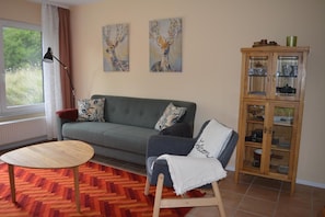 Uma sala de estar com sofá, mesa de centro redonda de madeira, aparador com portas de vidro e duas pinturas na parede.