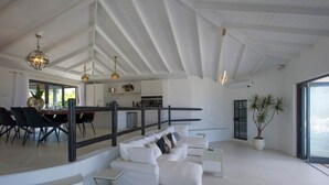 Ein geräumiger Wohnbereich mit einem weißen Sofa, einem Esstisch mit Stühlen, einer Treppe und einem großen Fenster.
