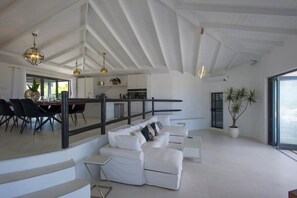 Ein geräumiger Wohnbereich mit einem weißen Sofa, einem Esstisch mit Stühlen, einer Treppe und einem großen Fenster.