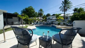 Ein Pool mit Liegestühlen und einem Tisch, umgeben von Palmen und Häusern.