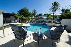 Ein Pool mit Liegestühlen und einem Tisch, umgeben von Palmen und Häusern.