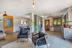 A modern kitchen with built-in appliances, a dining area with a table and chairs, and a living area with a sofa and a potted plant.