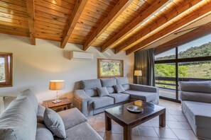 A modern living room with a grey sofa set, a wooden coffee table, and a large window offering a view of the outdoors.