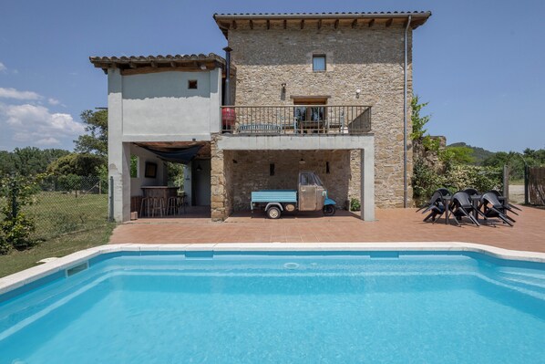 A two-story stone house with a swimming pool, a balcony, and outdoor seating.