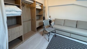 Una habitación con un armario de madera, una silla, un sofá y una alfombra estampada.