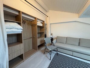 A room with a wooden wardrobe, a chair, a sofa, and a patterned rug. - Cozy apartment 2 min walk to beach - 4 guests (Anglet)