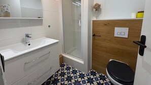Un baño con lavamanos blanco, espejo, ducha e inodoro.