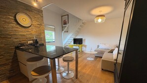 Una cocina moderna con pared de piedra, una zona de comedor con taburetes, una escalera y un salón con sofá.