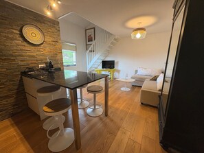 A modern kitchen with a stone wall, a dining area with stools, a staircase, and a living room with a sofa. - Cozy apartment 2 min walk to beach - 4 guests (Anglet)