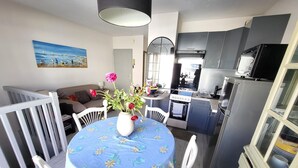 Un comedor con una mesa lista para dos, una cocina con electrodomésticos modernos y una sala de estar con un sofá y un cuadro en la pared.