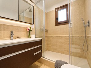 Une salle de bain moderne avec une douche à parois de verre, un meuble-lavabo avec un miroir et une petite fenêtre.