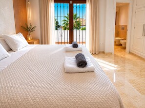 A hotel room with a large bed, a bathroom, and a view of palm trees. - House near the calm family beach (Estepona)
