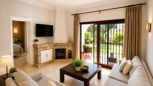 Una sala de estar con chimenea, televisor montado en la pared y vista al jardín a través de la puerta de vidrio.