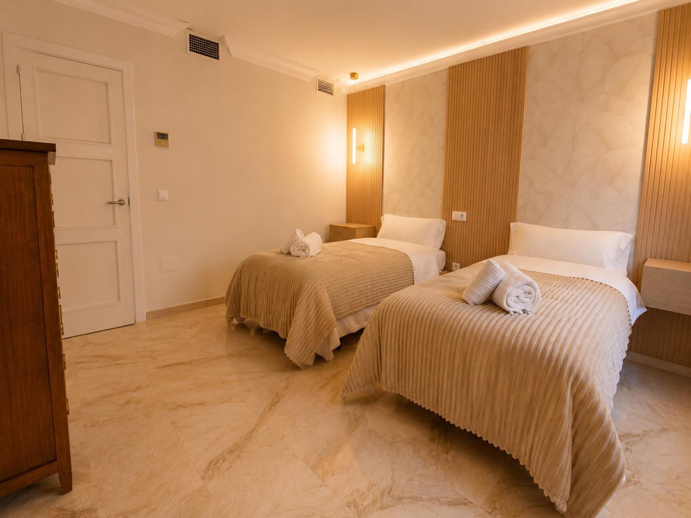 A hotel room with two beds, a wooden wardrobe, a white door, and a marble floor.