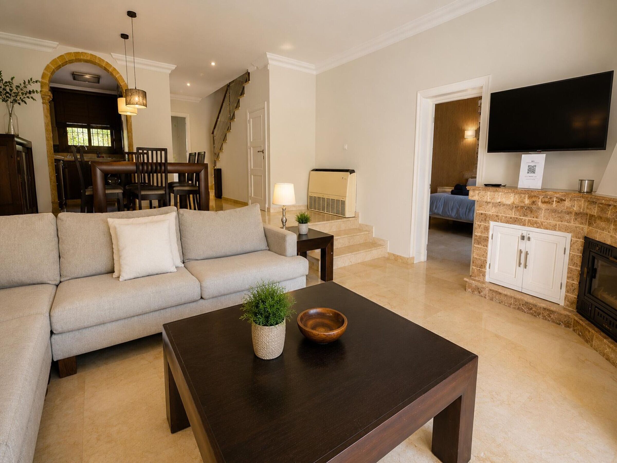 A living room with a sofa, a coffee table, a fireplace, a TV, and a staircase leading to a dining area.