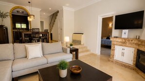 Una sala de estar con sofá, mesa de centro, chimenea, televisor y una escalera que lleva a un comedor.