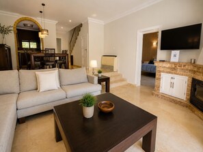 A living room with a sofa, a coffee table, a fireplace, a TV, and a staircase leading to a dining area. - House near the calm family beach (Estepona)