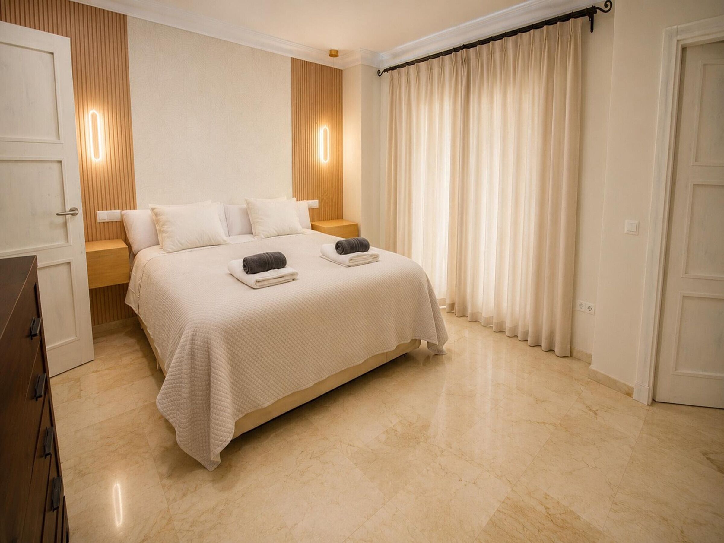 Une chambre d’hôtel avec un lit, des tables de chevet, une armoire et un rideau.