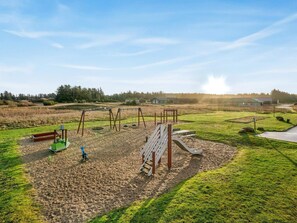 Ein Spielplatz mit Schaukeln und Rutsche, umgeben von Rasenflächen und Gebäuden im Hintergrund.