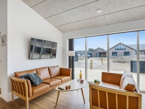 Ein modernes Wohnzimmer mit Ledersofa, Couchtisch und großem Fenster mit Blick auf einen Gebäudekomplex.