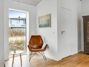Ein Zimmer mit Holzboden, einem braunen Ledersessel, einem kleinen runden Tisch mit einem Glas, einer Tür und einem Gemälde an der Wand.