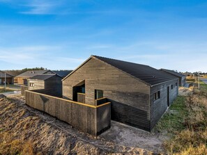 Een modern houten gebouw met een schuin dak, een omheind terras en een heldere lucht.