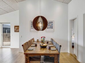 Ein Essbereich mit Holztisch, Korbstühlen, einer zentralen Leuchte und gerahmten Bildern an der Wand.