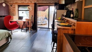 Een kleine keuken met een eethoek, een rode stoel en uitzicht door een glazen deur op een terras.