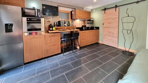 Een moderne keuken met een ingebouwde oven, magnetron en een flatscreen televisie. Houten kastjes, een bar met barkrukken en een groot raam.