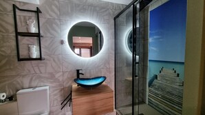 Een moderne badkamer met een ronde spiegel, een blauwe wastafel en een glazen douchecabine.