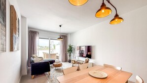 A modern living room with a sofa, dining table, and a TV. - Bright apartment, sea view - 4 guests (Estepona)