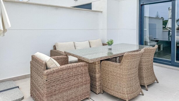 An outdoor patio with a glass table, wicker chairs, and a potted plant. - Bright apartment, sea view - 4 guests (Estepona)