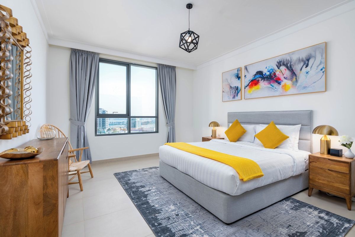 A modern bedroom with a large bed, a desk, and a view of the city.