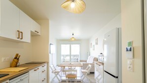 A modern kitchen with white cabinets, a wooden countertop, a dining table with chairs, and a hanging light fixture. - New apartment near ocean - 4 guests (Mimizan)