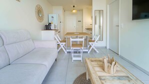 A modern living room with a sofa, a dining table with chairs, a kitchen area, and a TV mounted on the wall. - New apartment near ocean - 4 guests (Mimizan)