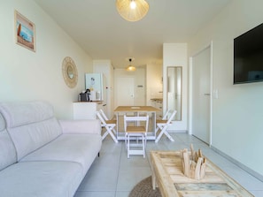Een moderne woonkamer met een bank, een eettafel met stoelen, een keuken en een aan de muur bevestigde televisie.
