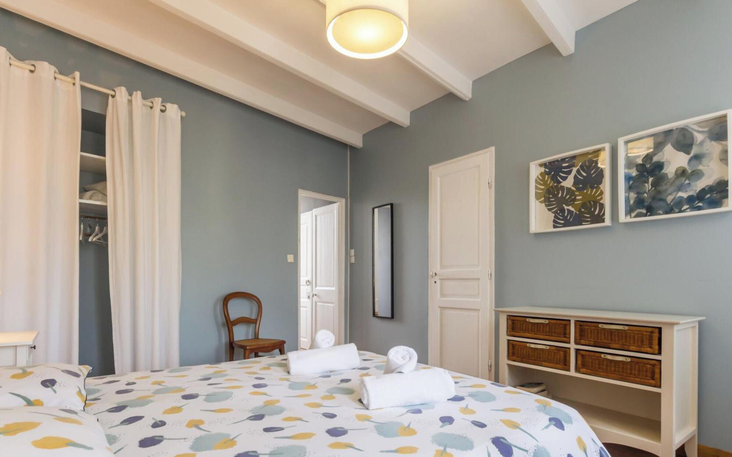 A bedroom with a bed, a wardrobe, a chair, a bedside table, and artwork on the wall.