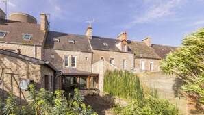 A stone building with multiple chimneys, a small attached structure with a roof, and a garden area with various plants.