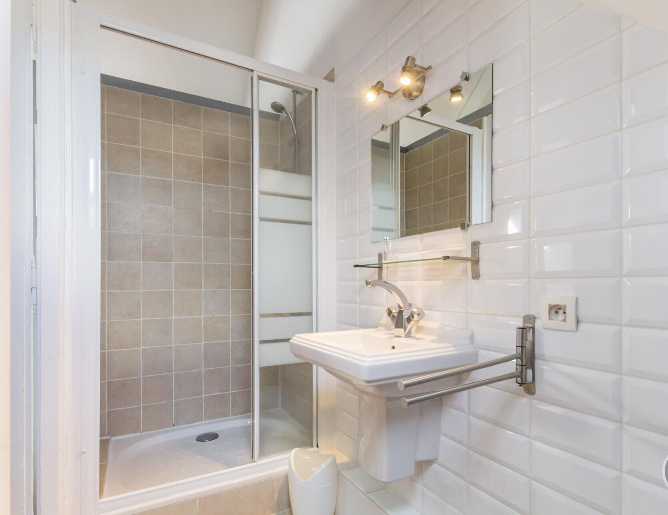 Une salle de bain avec une douche à parois de verre, un lavabo blanc avec un porte-serviettes et un miroir au-dessus du lavabo.