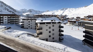 En snedækket bjergby med moderne bygninger, heriblandt et hotel med balkoner og en skibakke i baggrunden.