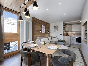 Eine moderne Küche mit eingebauten Geräten, ein Essbereich mit Holztisch und -stühlen und Bergblick durch ein großes Fenster.