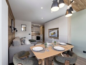 Ein moderner Essbereich mit einem Holztisch, gedeckt für vier Personen, einer Couch und einer Küche im Hintergrund.