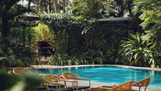 Ein Pool mit Liegestühlen und Tischen, umgeben von dichtem tropischen Grün.