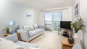 A modern living room with a sofa, TV, and a balcony with a view. - 18 The Sands - Sea View, Parking, Family friendly (Carbis Bay)