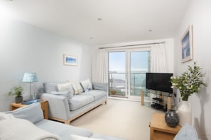 Ein modernes Wohnzimmer mit Sofa, Fernseher und einem Balkon mit Blick.