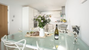 A modern kitchen with white cabinets, a dining table with chairs, and a vase of flowers. - 18 The Sands - Sea View, Parking, Family friendly (Carbis Bay)