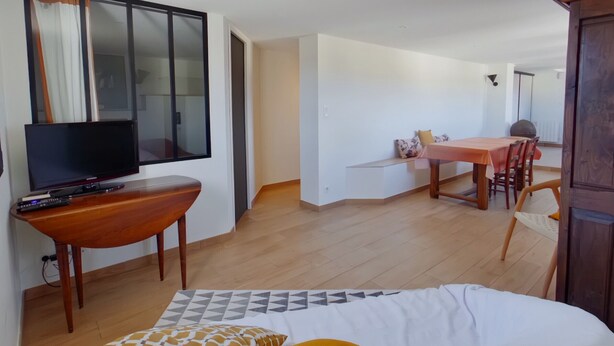 Ein Hotelzimmer mit Bett, Fernseher auf einem Holztisch, einem Esstisch mit Stühlen und einem großen Fenster mit Vorhängen.